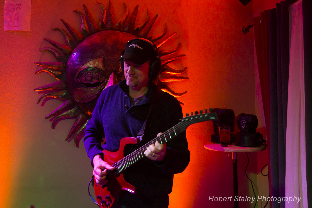 Russell playing a red electric guitar in front of a big sun sculpture